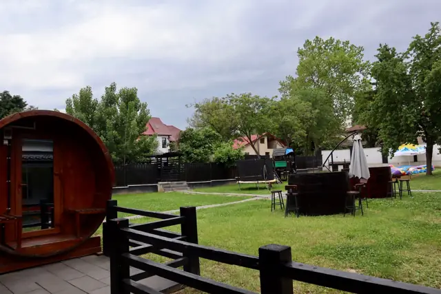 Sauna-butoi lângă gardul de lemn, cu curtea în spate